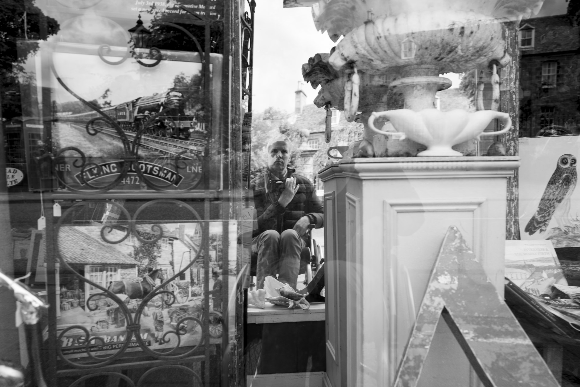 Black and white selfie style image of a man looking into a shop window filled with antiques